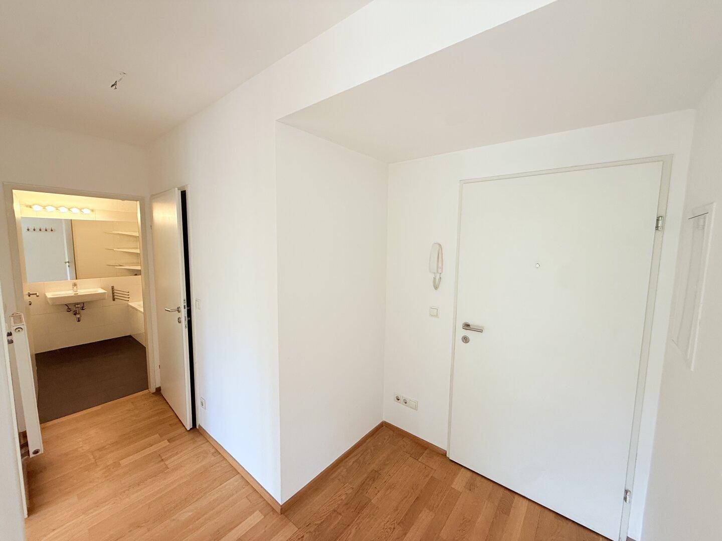 Heller Eingangsbereich mit Holzparkett und Zugang zu einem Badezimmer.