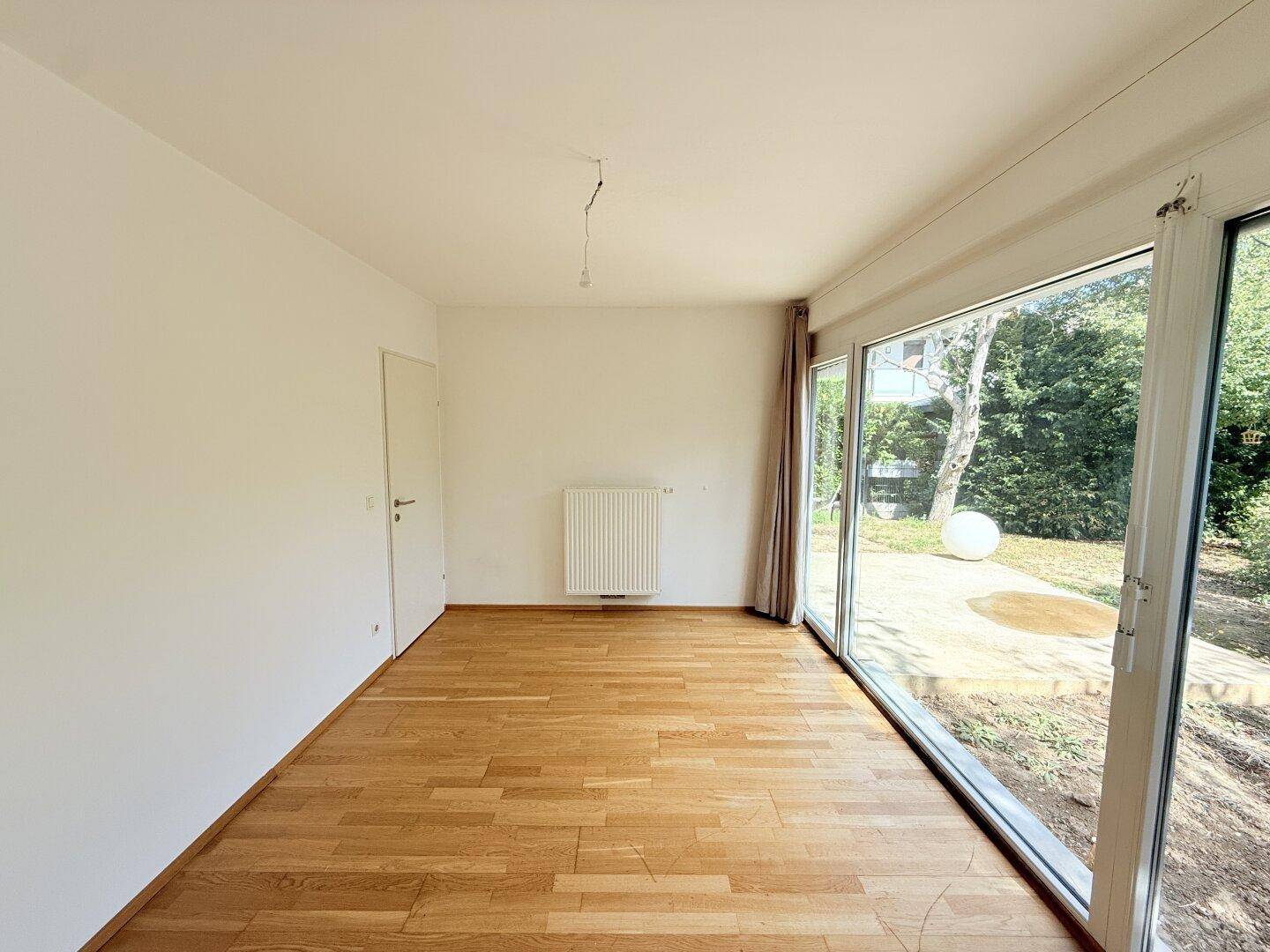 Geräumiges Zimmer mit Holzparkett und großen Fenstern, die viel Licht hereinlassen.