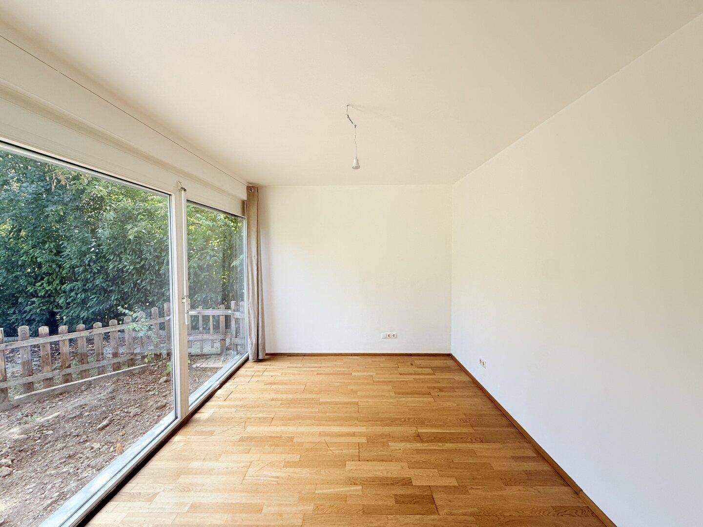 Heller Wohnraum mit Holzparkett und breiter Fensterfront zum Garten.