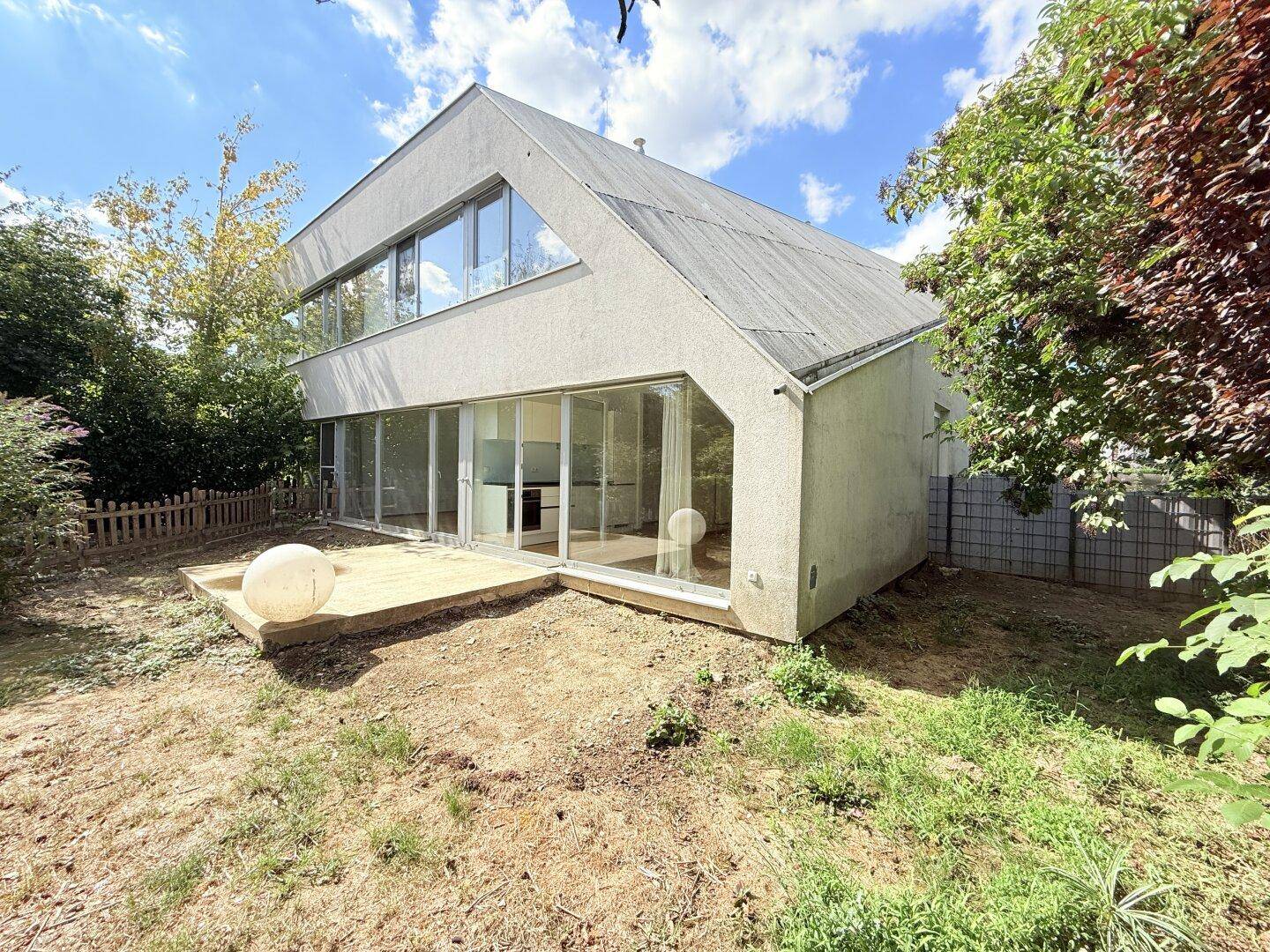 Modernes Haus mit großen Fensterfronten und einer Terrasse im Garten.