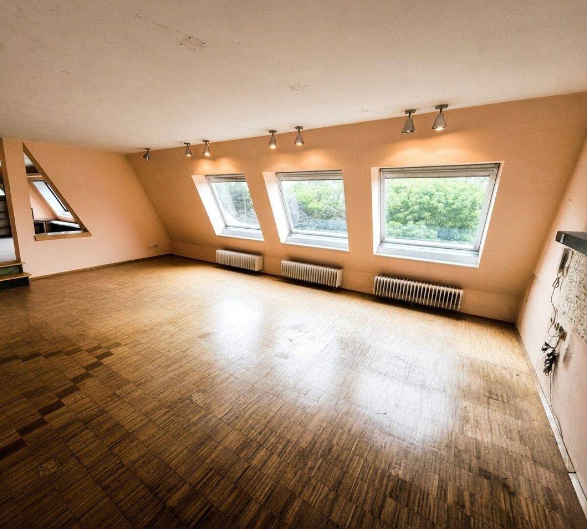 Heller Dachgeschossraum mit schrägen Wänden, Holzparkettboden und Dachfenstern.