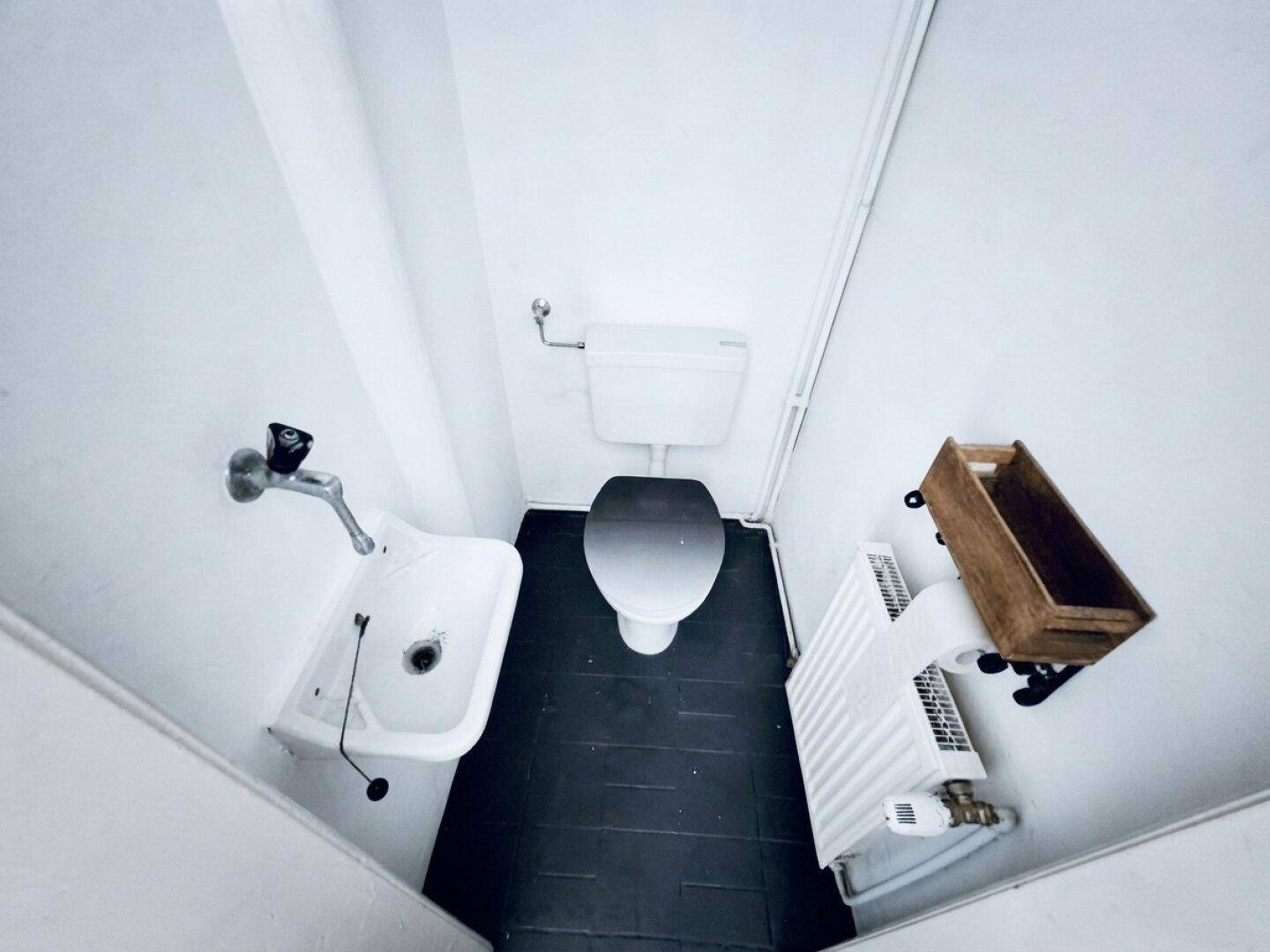 Kleines Gäste-WC mit dunklen Fliesen, einfacher Toilette und einem traditionellen Waschbecken.