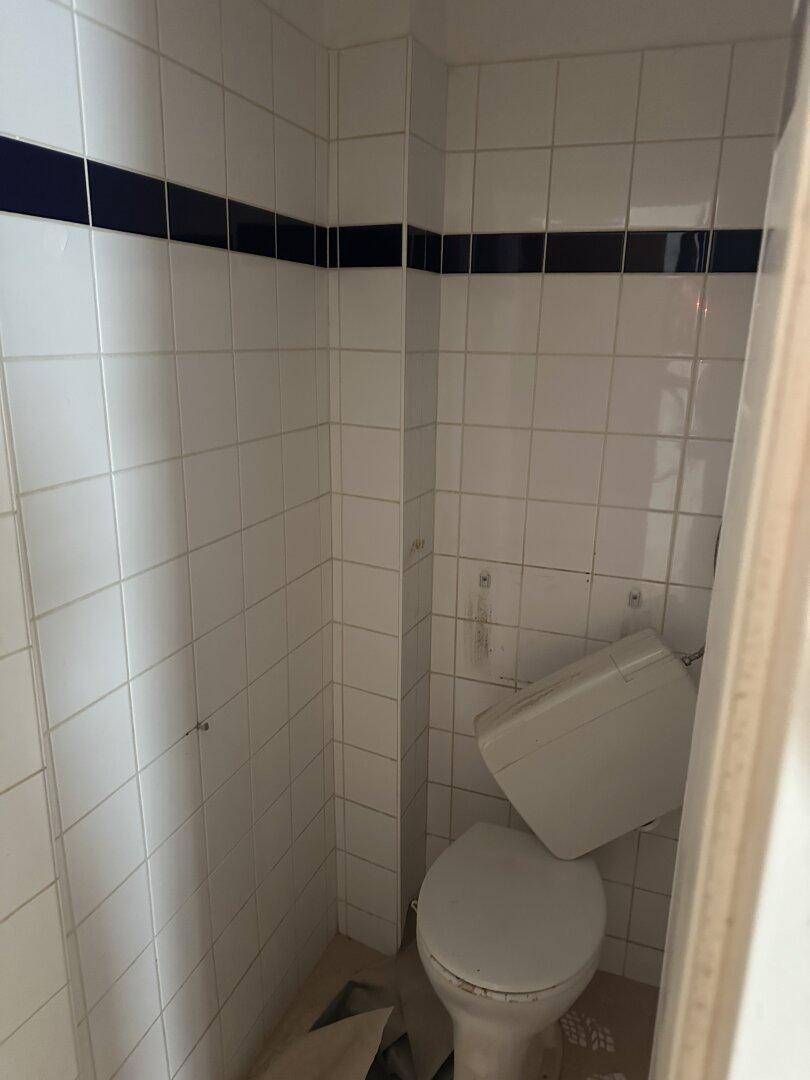 Kleines WC mit weißen Fliesen, einer blauen Zierleiste und einer einfachen Toilette.