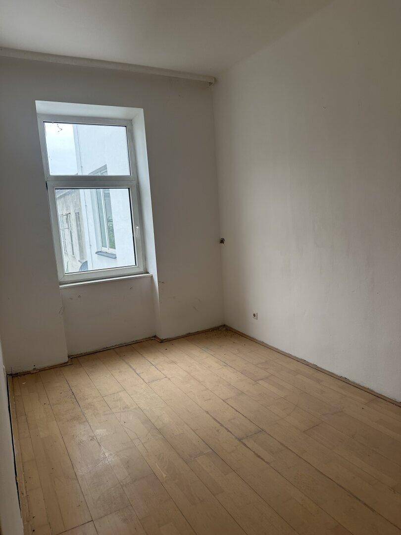 Leeres Zimmer mit einem Fenster und hellem Holzplankenboden, bereit zur Renovierung.