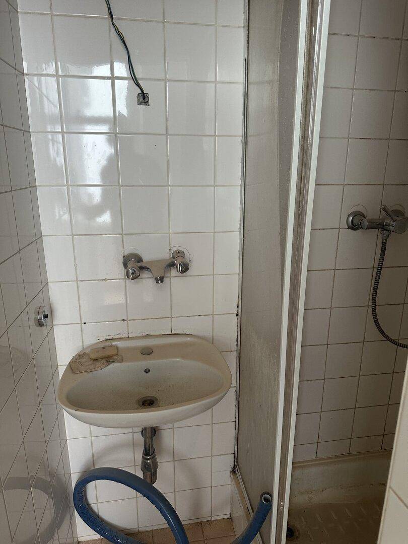 Kleines Badezimmer mit Waschbecken und Duschkabine, ausgestattet mit weißen Fliesen.