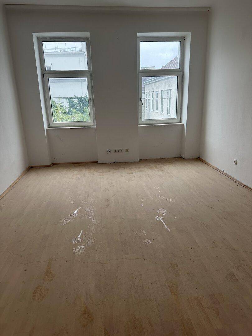 Leeres Zimmer mit zwei Fenstern und hellem Holzboden, bietet viel natürliches Licht.