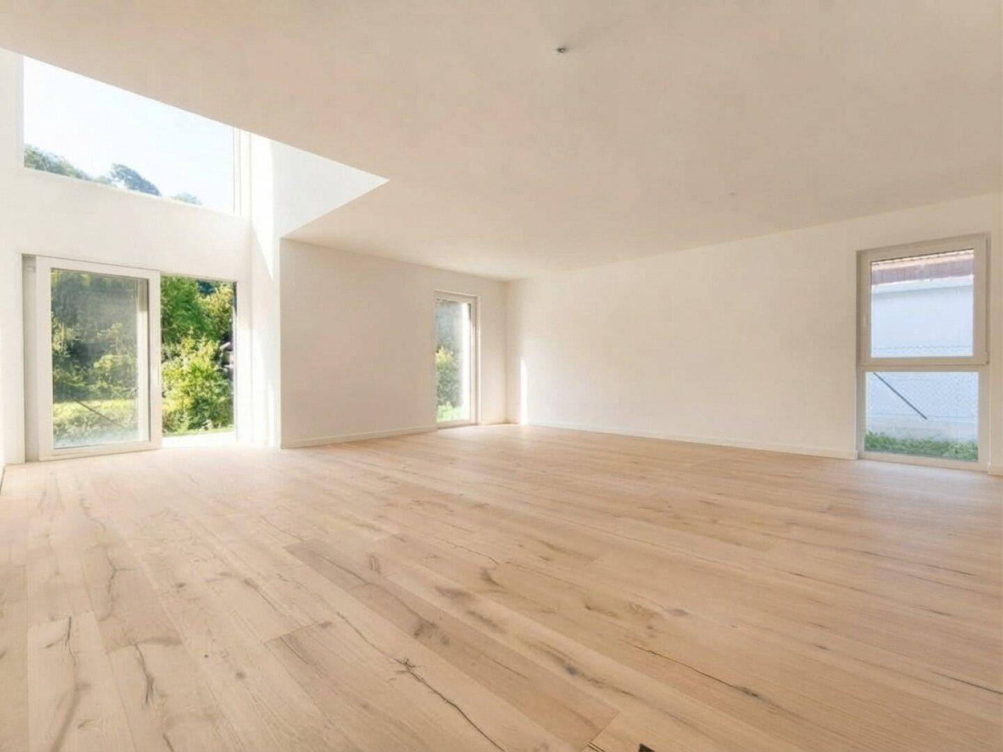 Helles, leeres Wohnzimmer mit großen Fenstern, Holzboden und viel natürlichem Licht.
