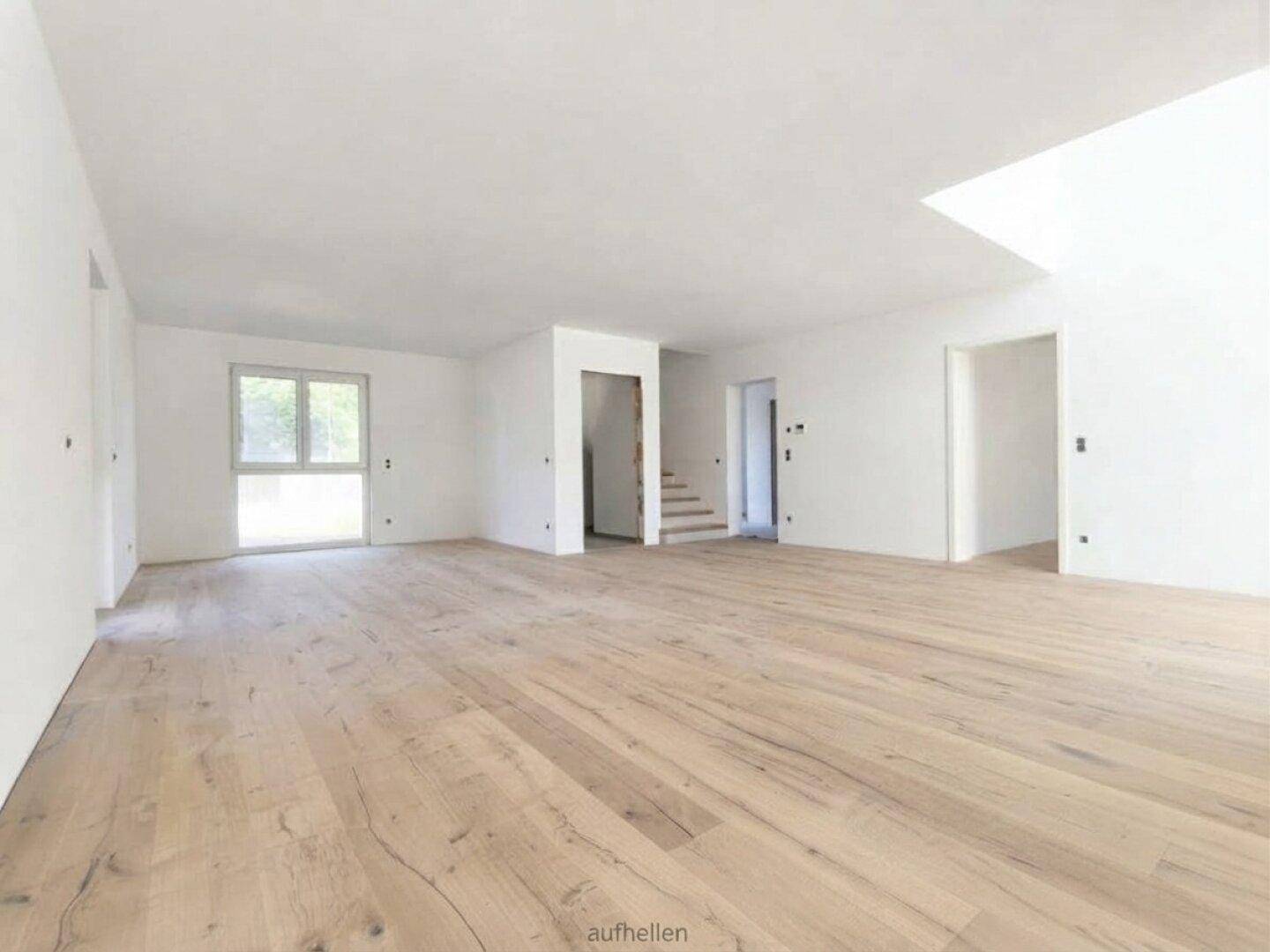 Geräumiges, leeres Wohnzimmer mit hellem Holzboden und Zugang zum Treppenbereich.