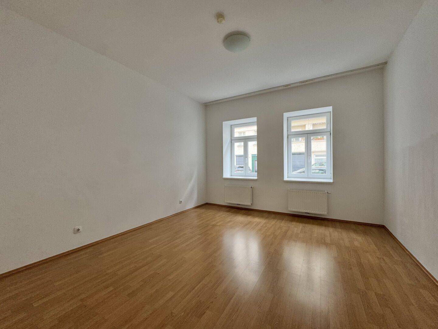 Leerer Raum mit Holzboden und zwei Fenstern, bereit zur individuellen Gestaltung.