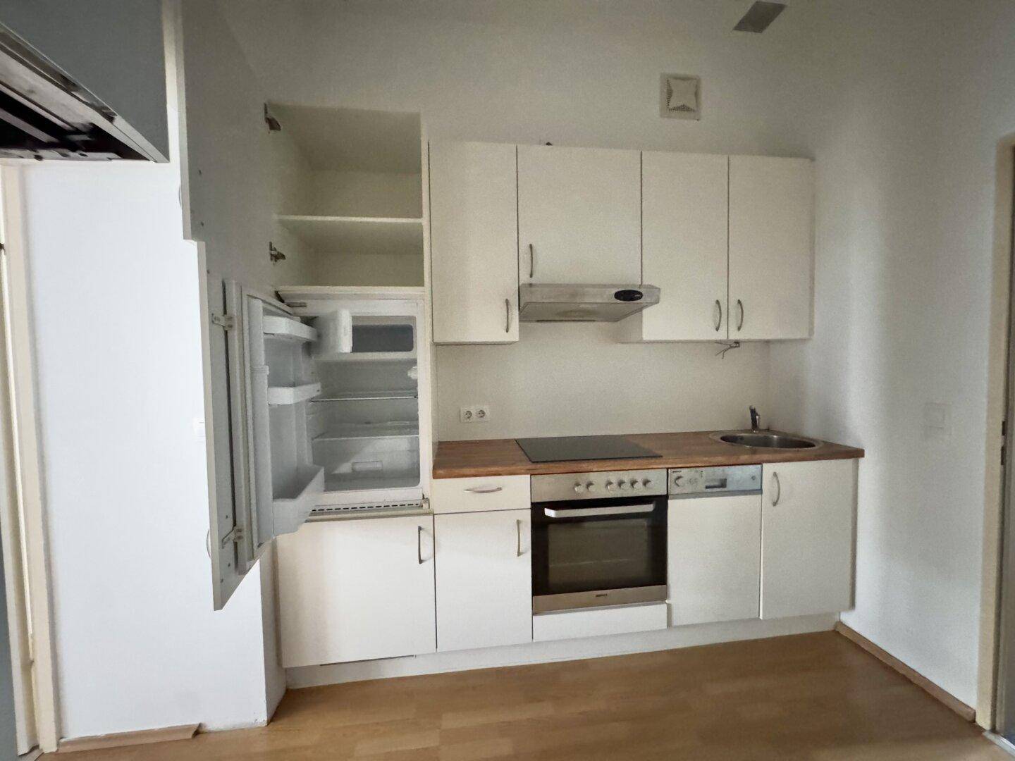 Kompakte Einbauküche mit weißen Schränken, Kühlschrank und Kochfeld.