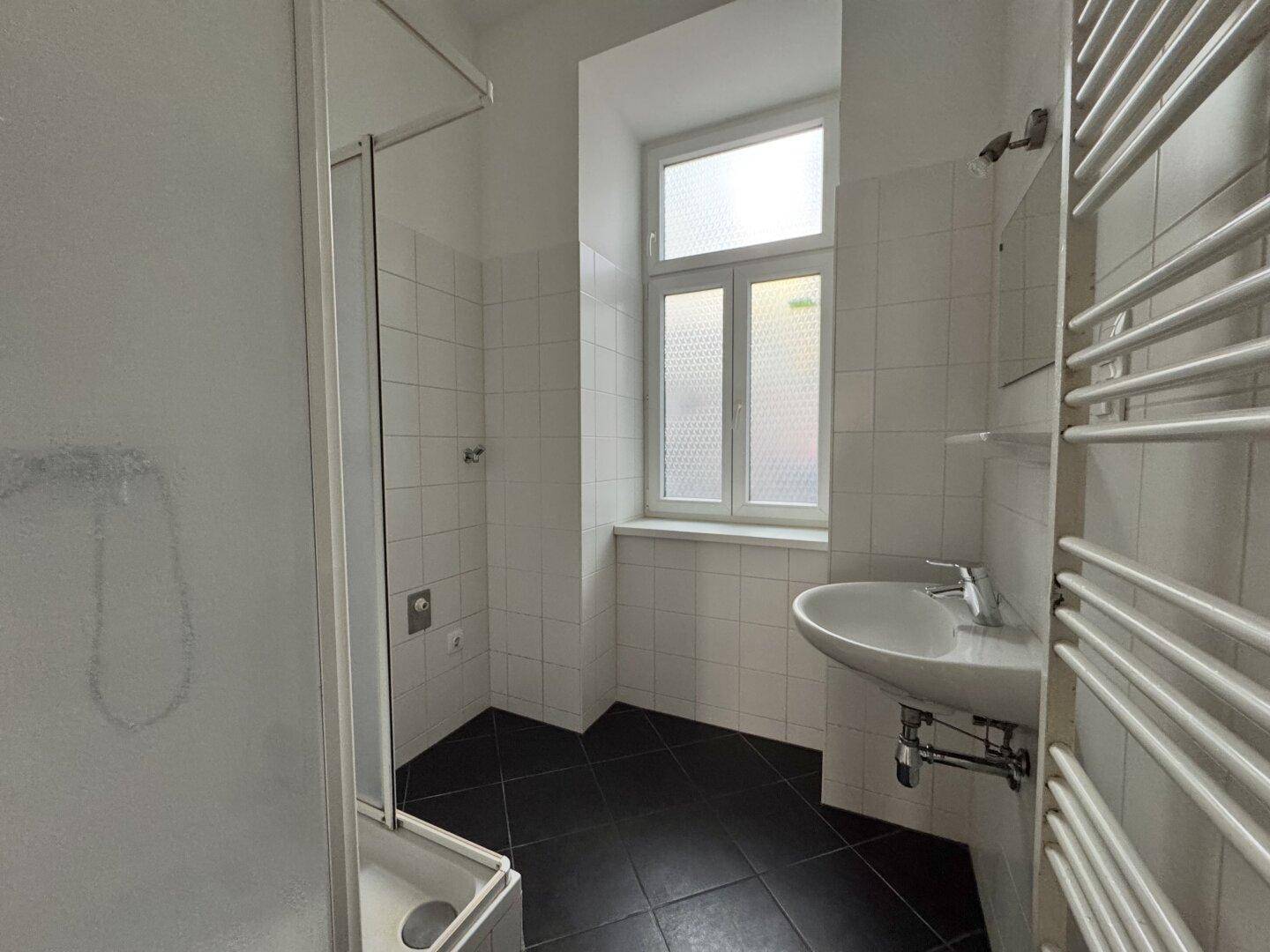 Modernes Badezimmer mit Dusche, Waschbecken, Fenster und beheiztem Handtuchhalter.