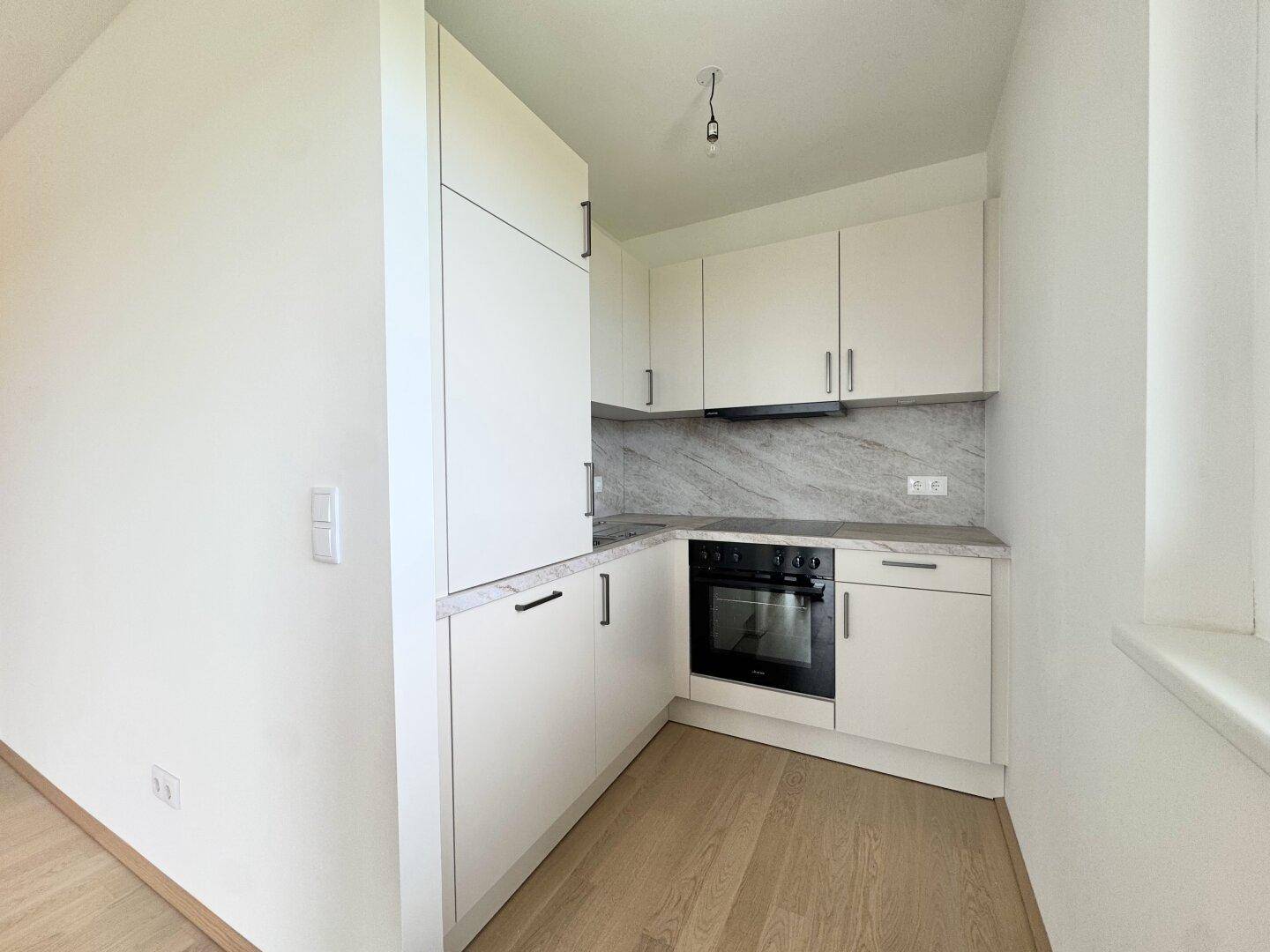 Moderne Einbauküche in Weiß mit hellem Holzboden, integriertem Backofen und Marmor-Optik-Rückwand.