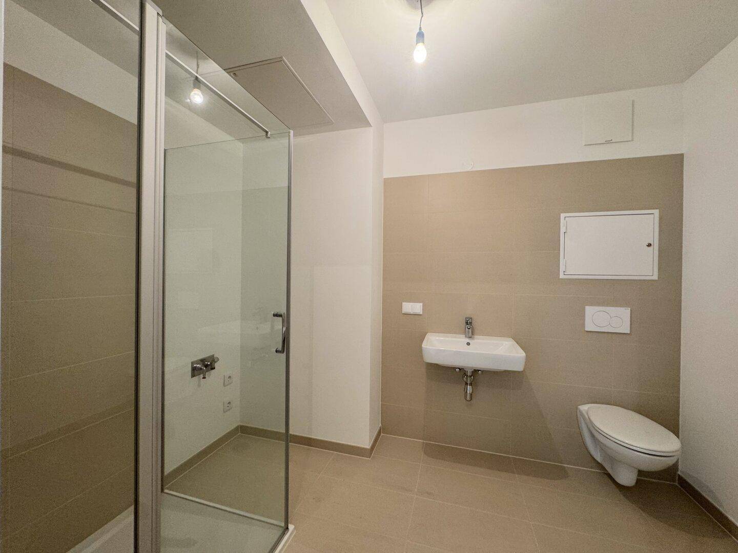 Modernes Badezimmer mit begehbarer Dusche, Wand-WC und hellen Fliesen an Wänden und Boden.