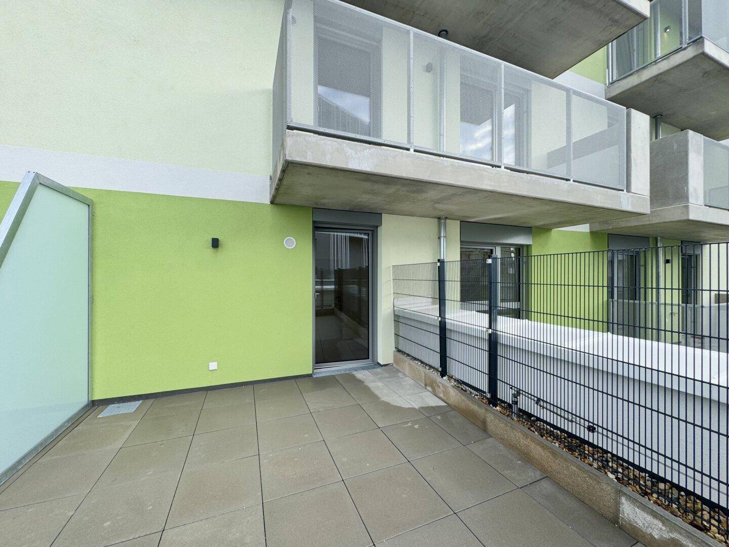 Helle Terrasse mit Fliesenboden und Zugang zum Innenbereich, umgeben von einer modernen Fassade.