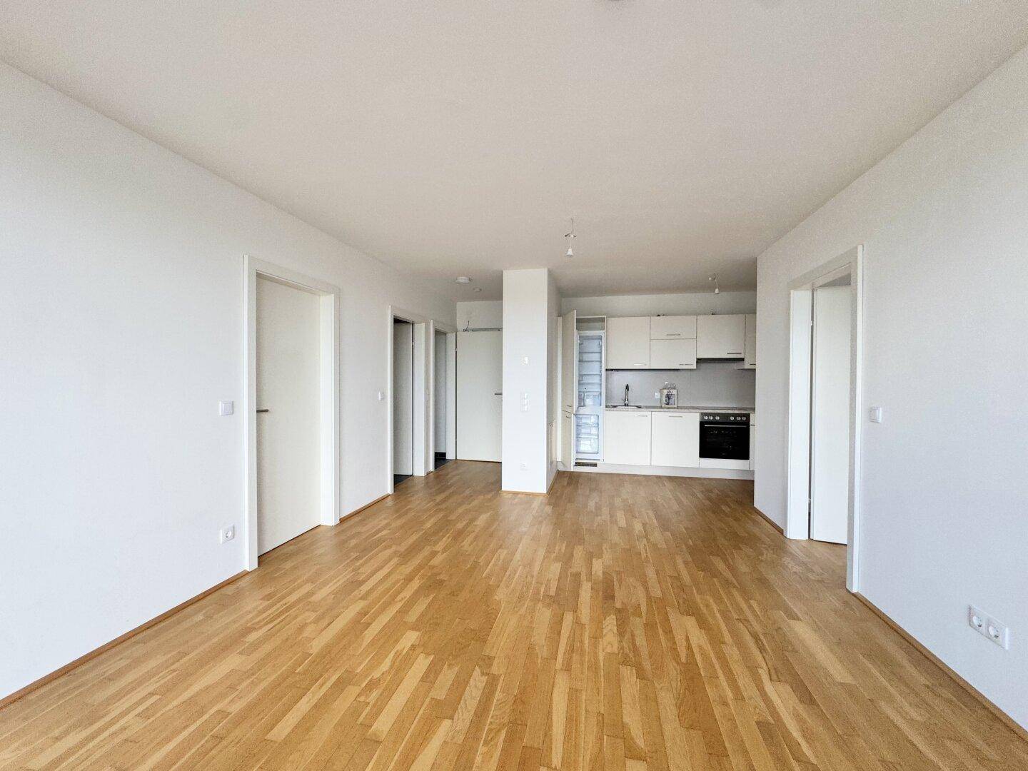 Offener Wohnbereich mit Parkettboden und integrierter, moderner Küchenzeile im Hintergrund.