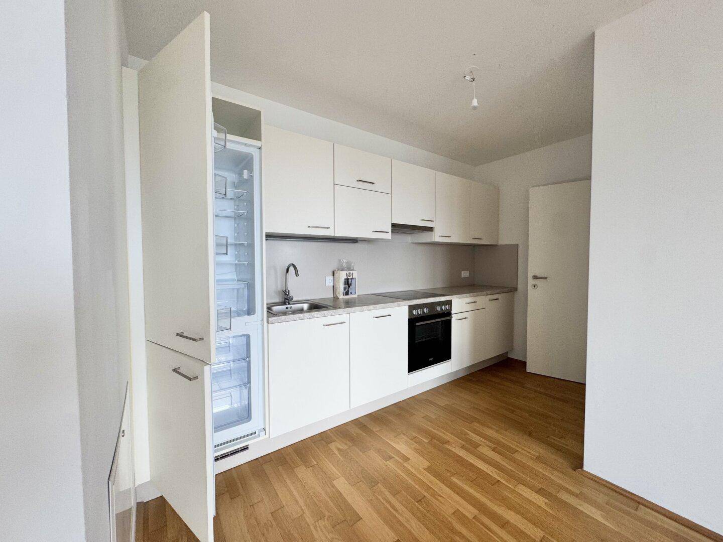 Moderne Einbauküche mit weißen Hochglanzfronten, integriertem Kühlschrank und Backofen.