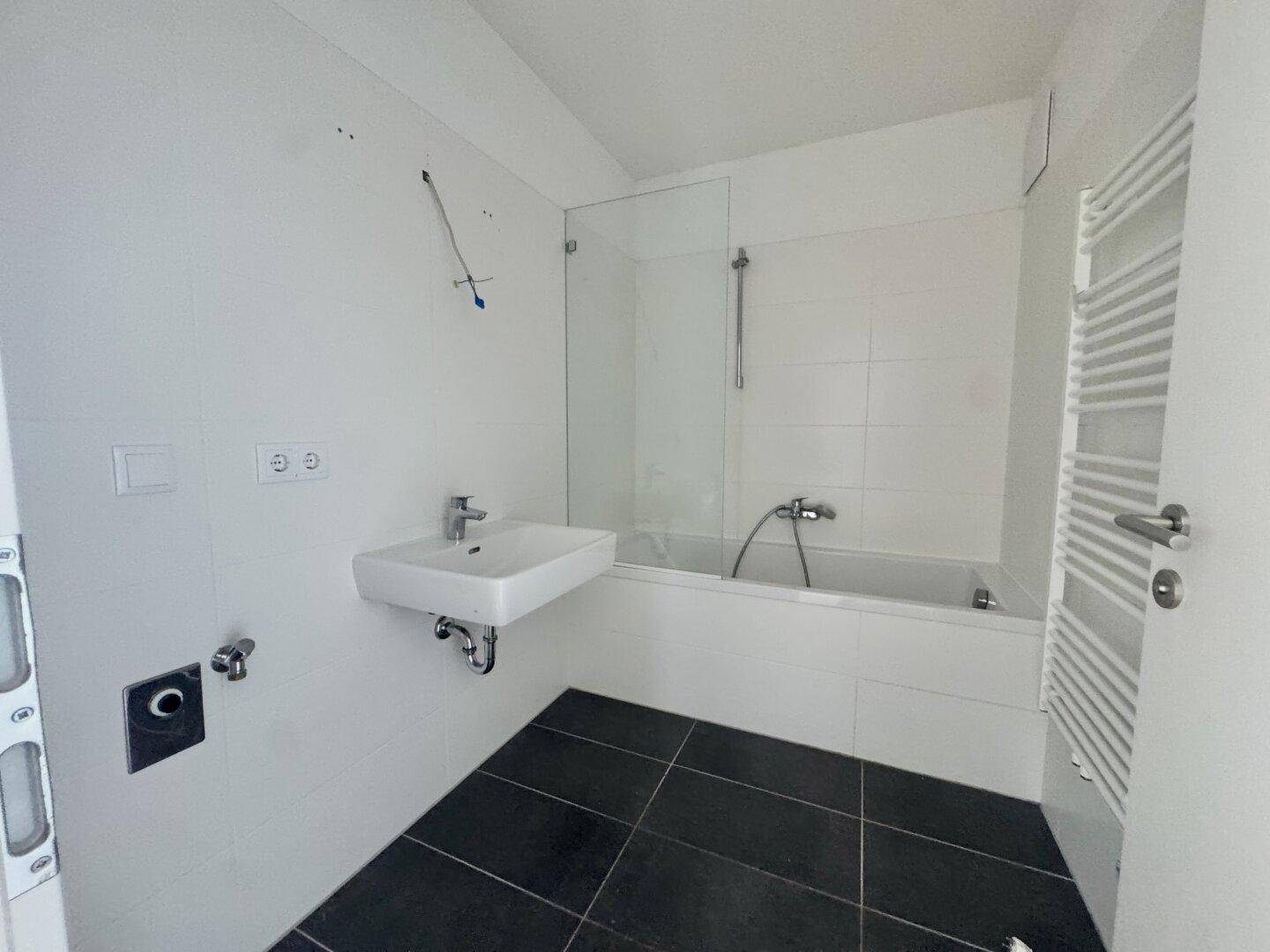 Modernes Badezimmer mit weißen Fliesen, Badewanne, Duschwand, Waschbecken und Handtuchheizkörper.