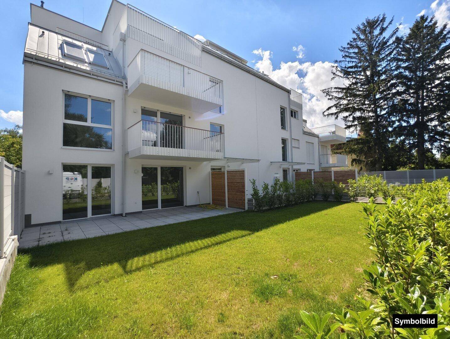 Gepflegter Gartenbereich mit Rasenfläche und einer Terrasse vor der modernen Wohnanlage.