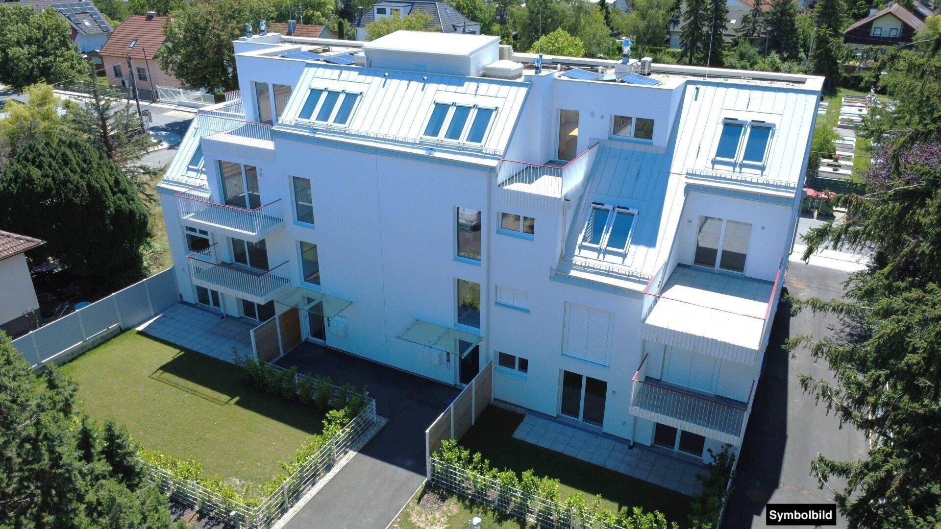Luftaufnahme einer modernen Wohnanlage mit weißer Fassade und Dachfenstern in grüner Umgebung.