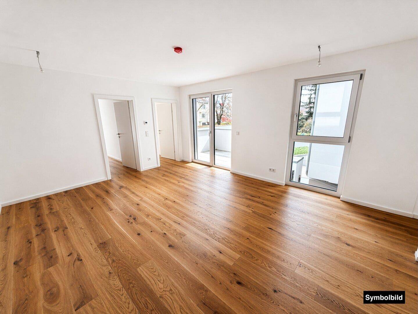 Heller Wohnraum mit Eichenparkettboden, weißen Wänden und Zugang zu einem Balkon.