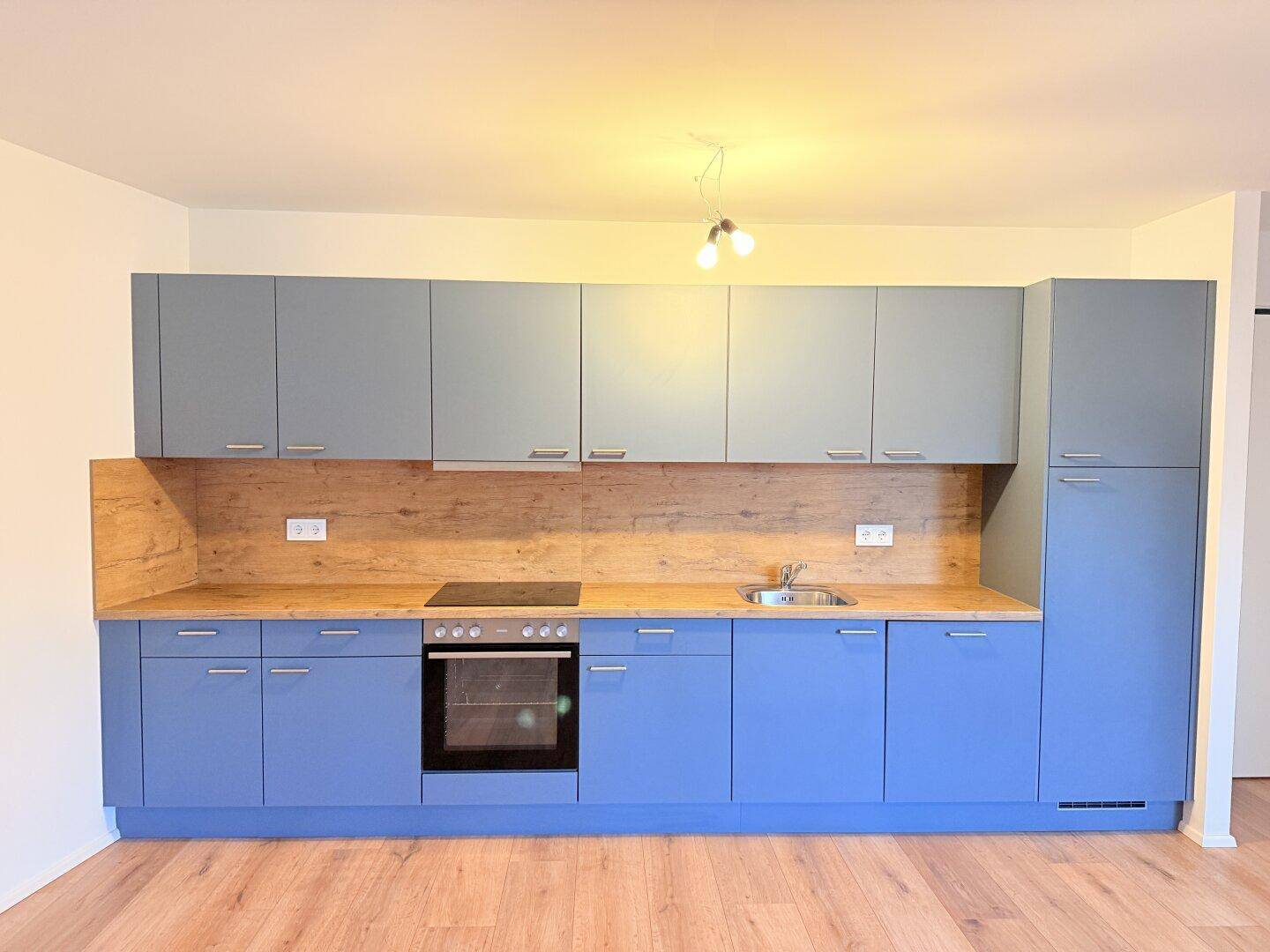 Moderne Einbauküche in Blau- und Grautönen mit Holzarbeitsplatte und Kochfeld.