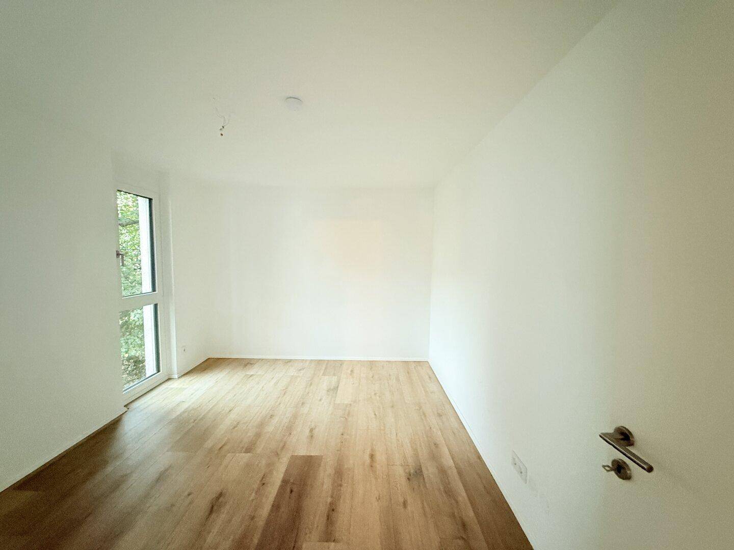 Helles Schlafzimmer mit Laminatboden und Fenster mit Blick ins Grüne.