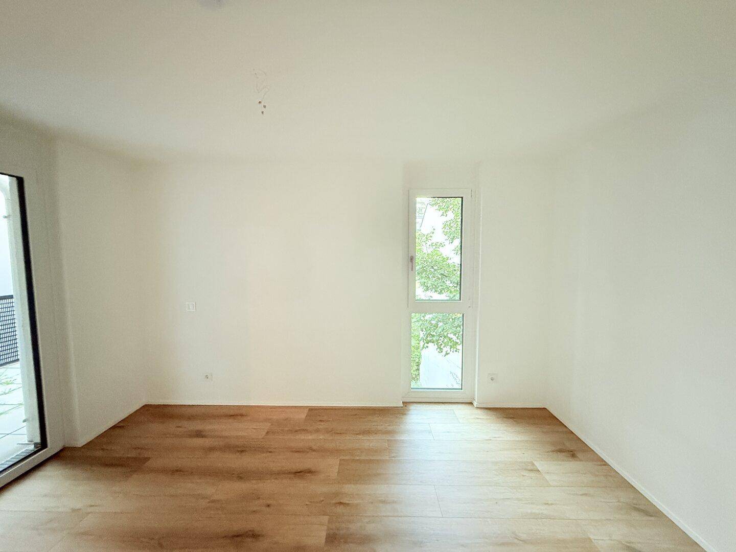 Geräumiges Schlafzimmer mit hellem Laminatboden und großem Fenster.