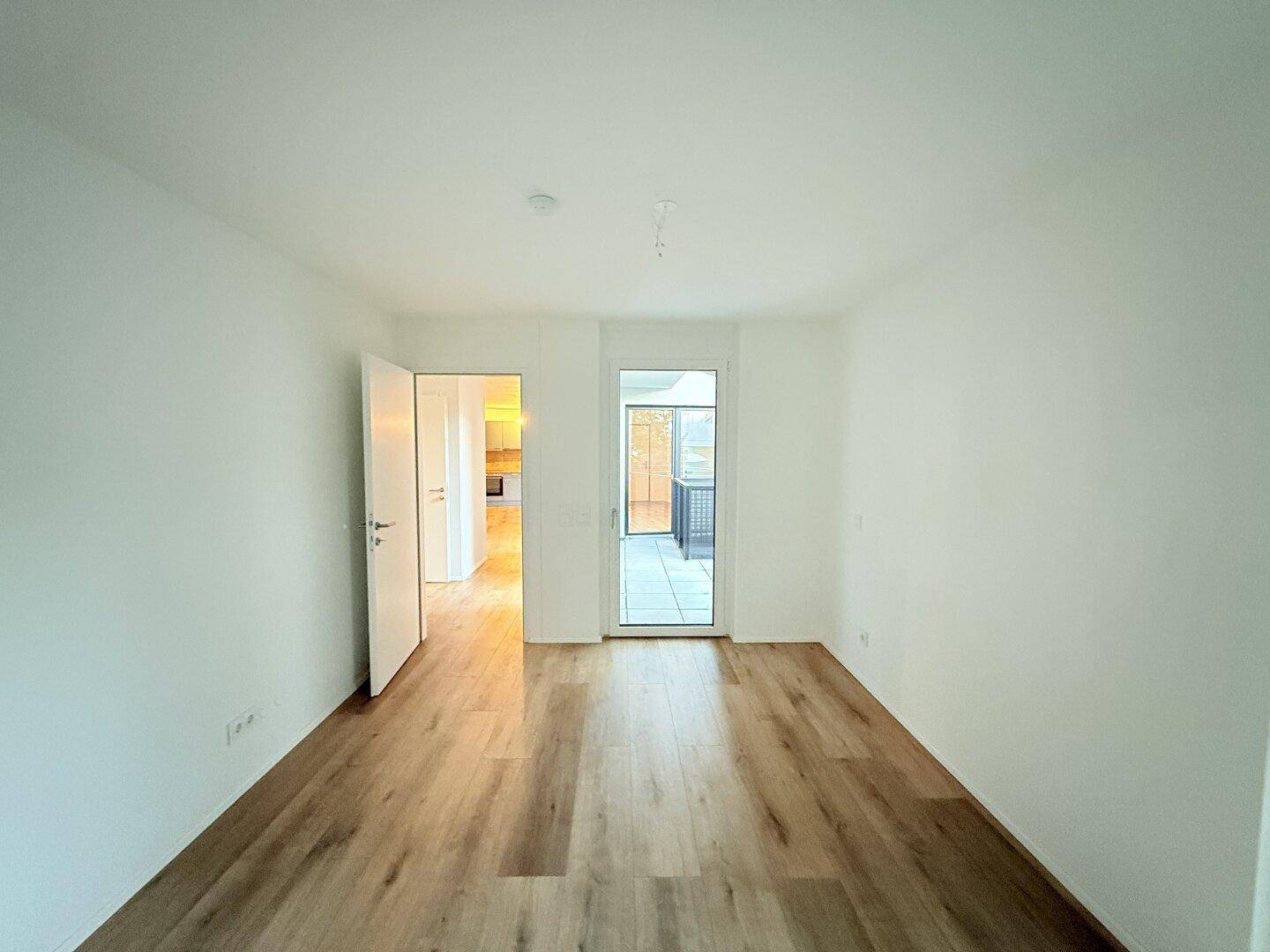 Schlafzimmer mit Laminatboden und Zugang zu einem weiteren Raum und Balkon.
