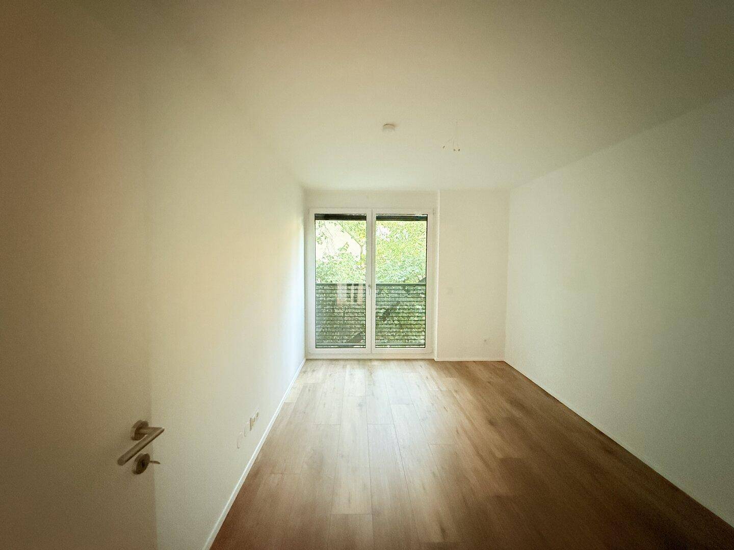 Schlafzimmer mit Laminatboden und großen Fenstern, die viel Licht hereinlassen.