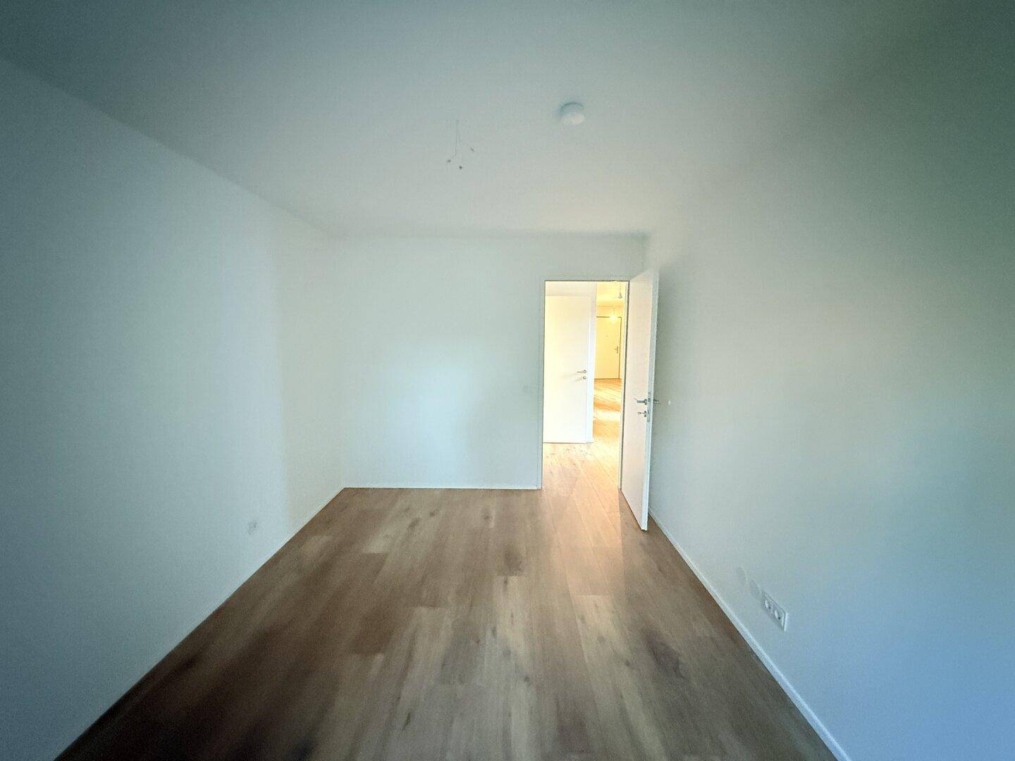 Helles Schlafzimmer mit Laminatboden und Zugang zu einem weiteren Raum.