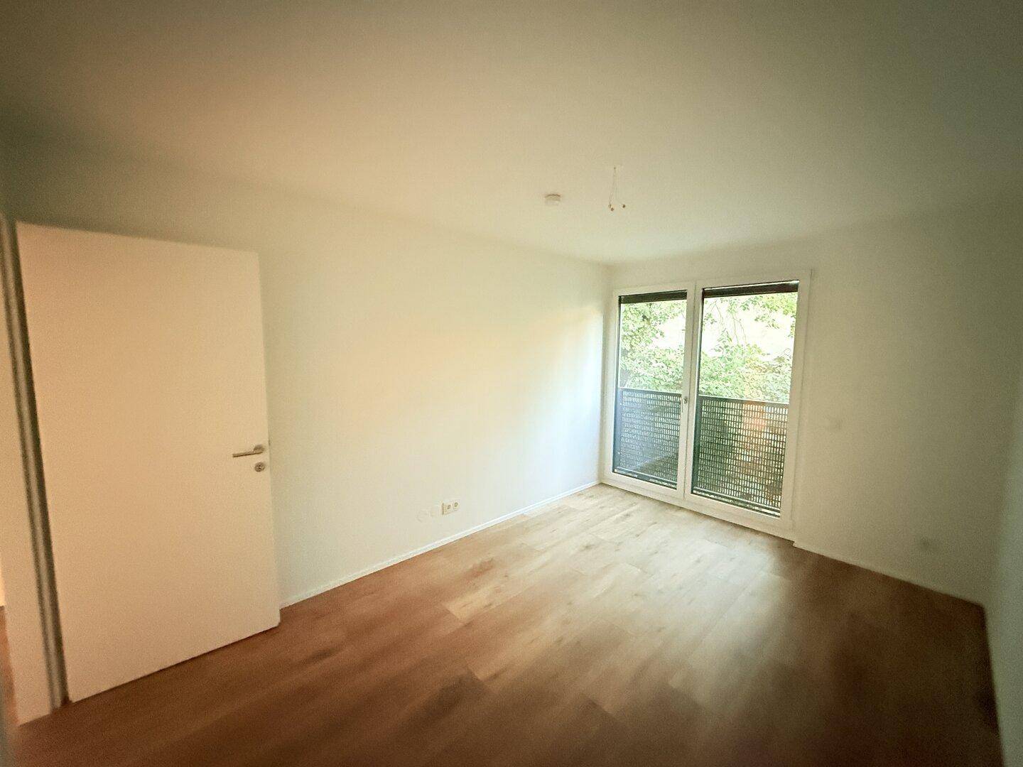 Geräumiges Schlafzimmer mit Laminatboden und großen Fenstern zum Balkon.