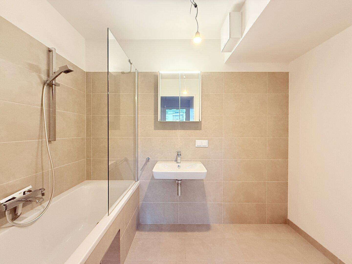 Modernes Badezimmer mit Badewanne, Duschabtrennung und beigefarbenen Fliesen.