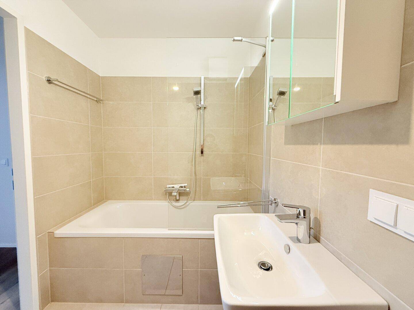 Helles Badezimmer mit Badewanne, Waschbecken und Spiegelschrank.