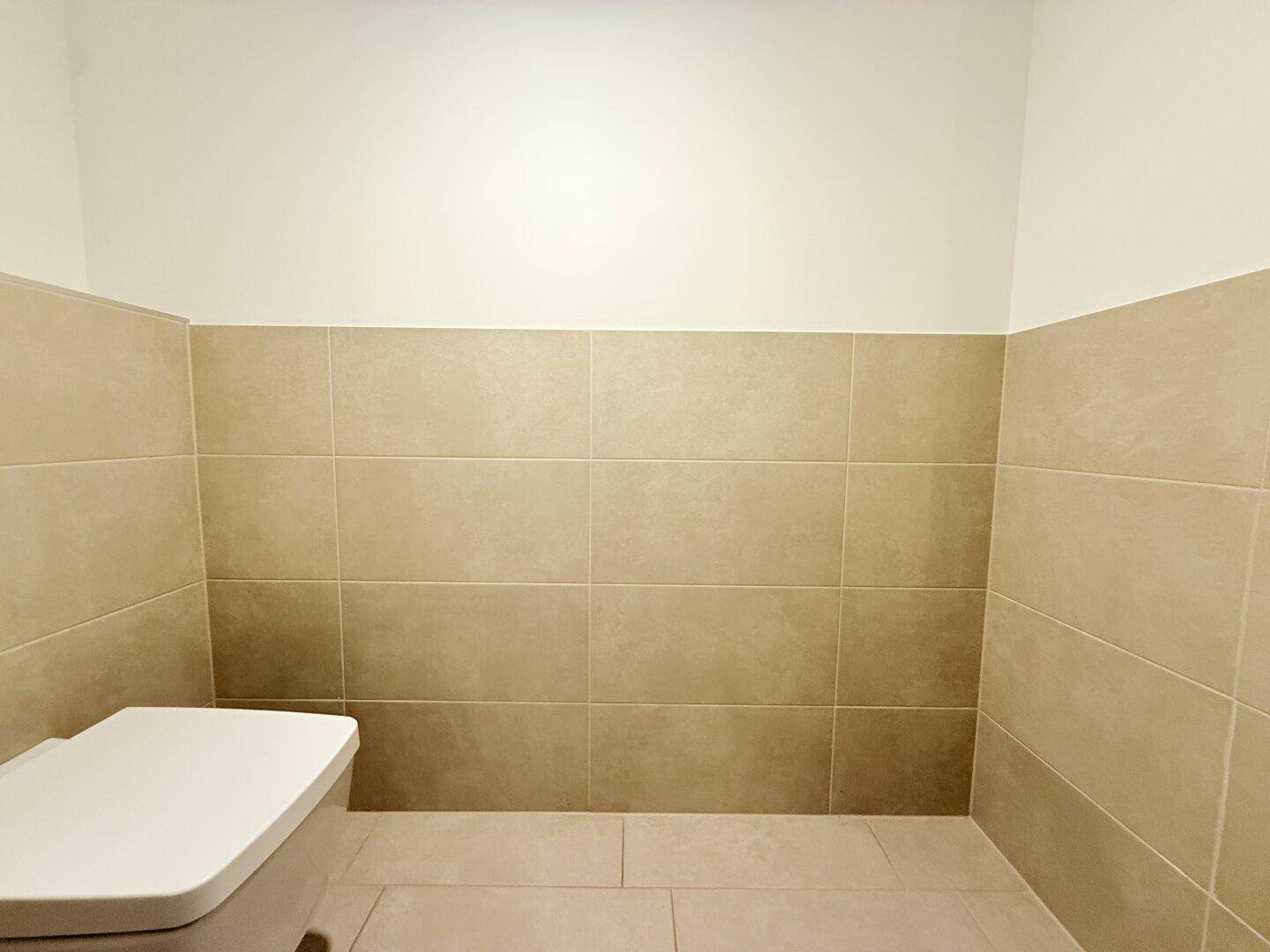 Separate Toilette mit beigefarbenen Fliesen und Wand-WC.