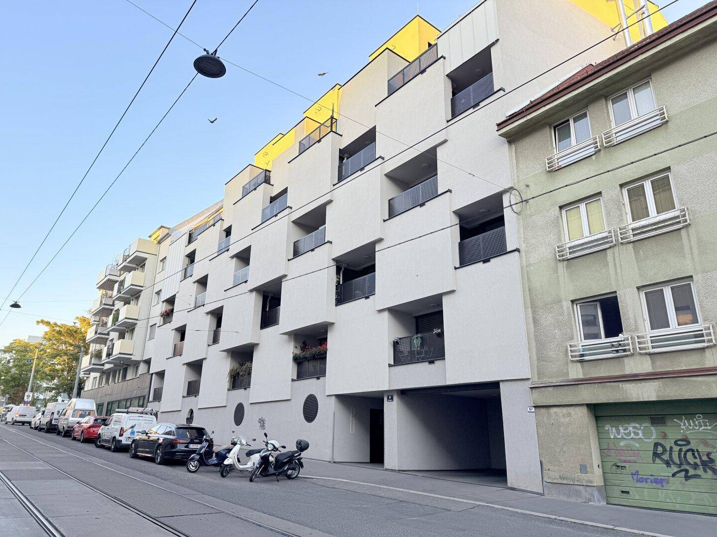 Moderne Wohnanlage mit mehreren Balkonen und einer hellen Fassade an der Straße.