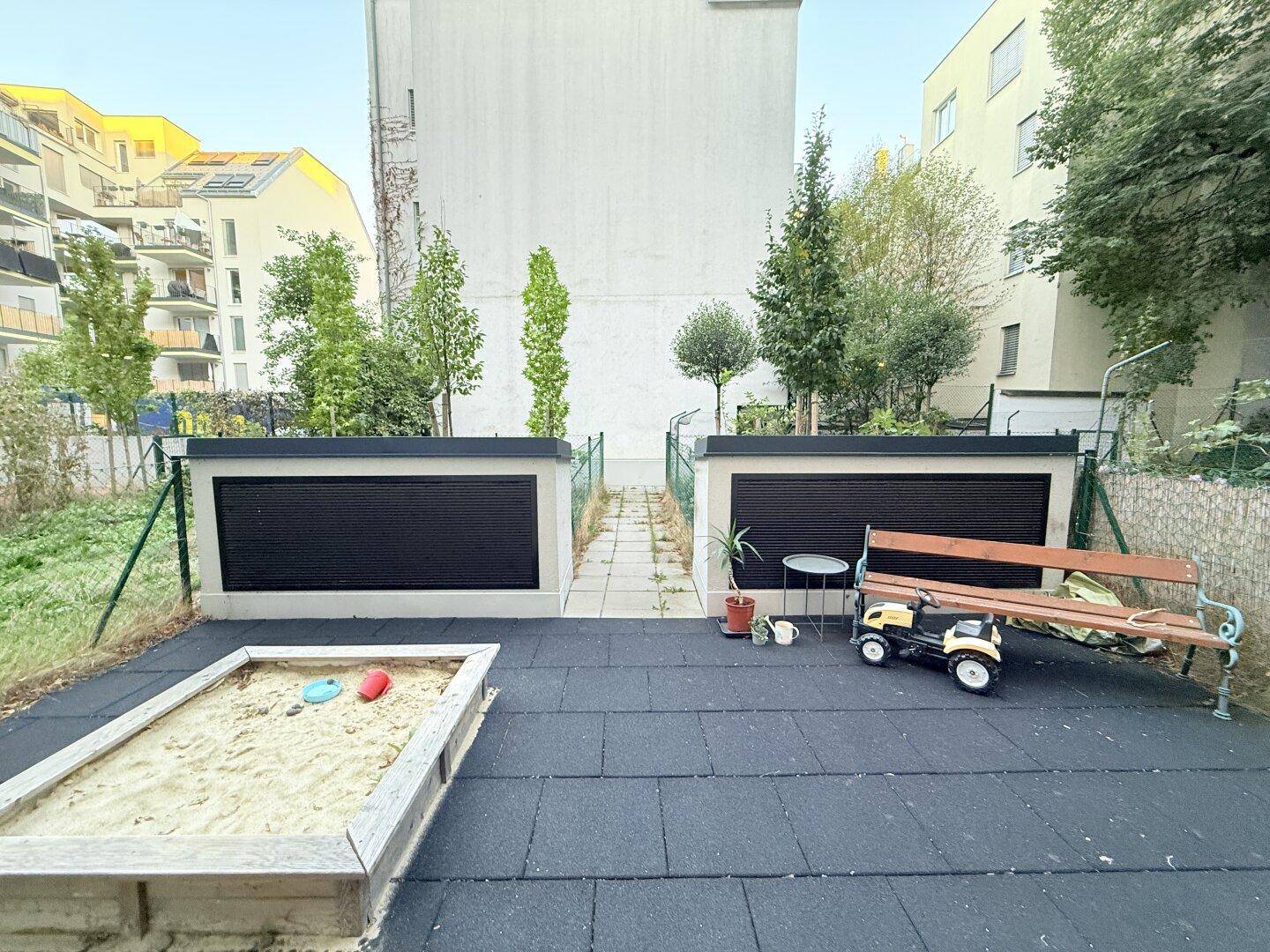 Gemeinschaftsgarten mit Sandkasten, Sitzbank und Bäumen im Innenhof.