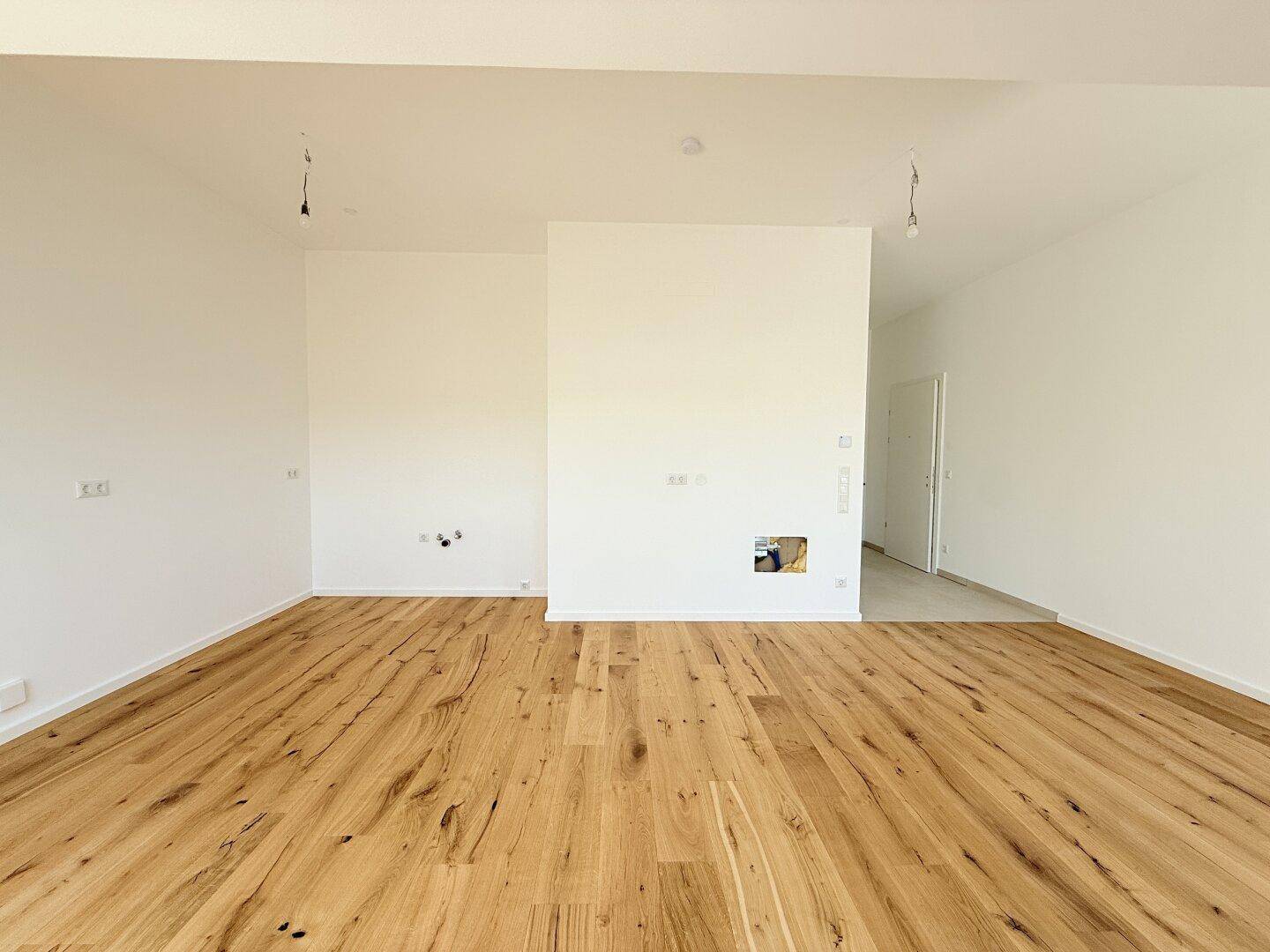 Helles, leeres Zimmer mit Holzboden und weißen Wänden, bereit für die individuelle Einrichtung.