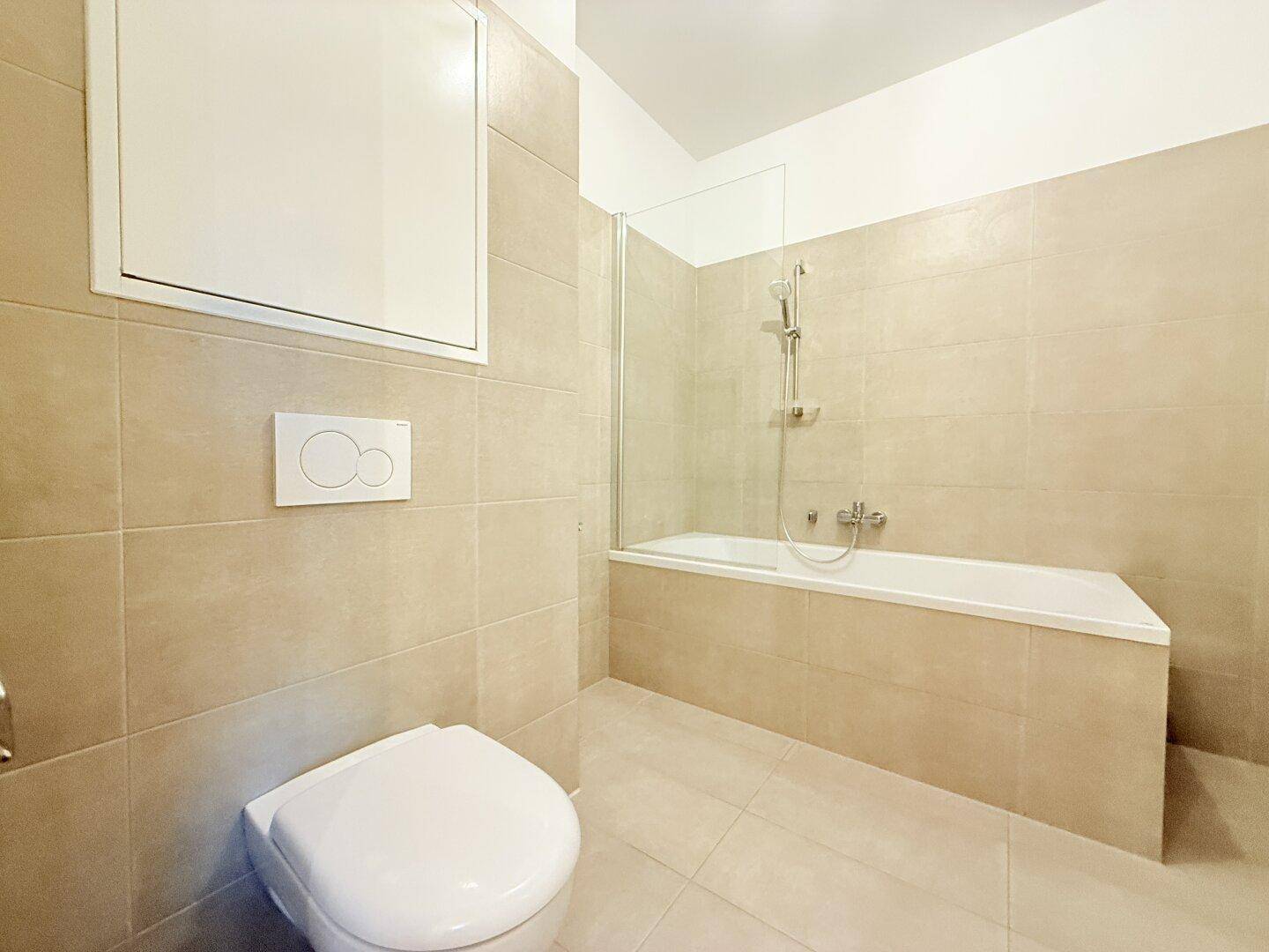 Helles Badezimmer mit beigefarbenen Fliesen, Badewanne und wandhängendem WC.