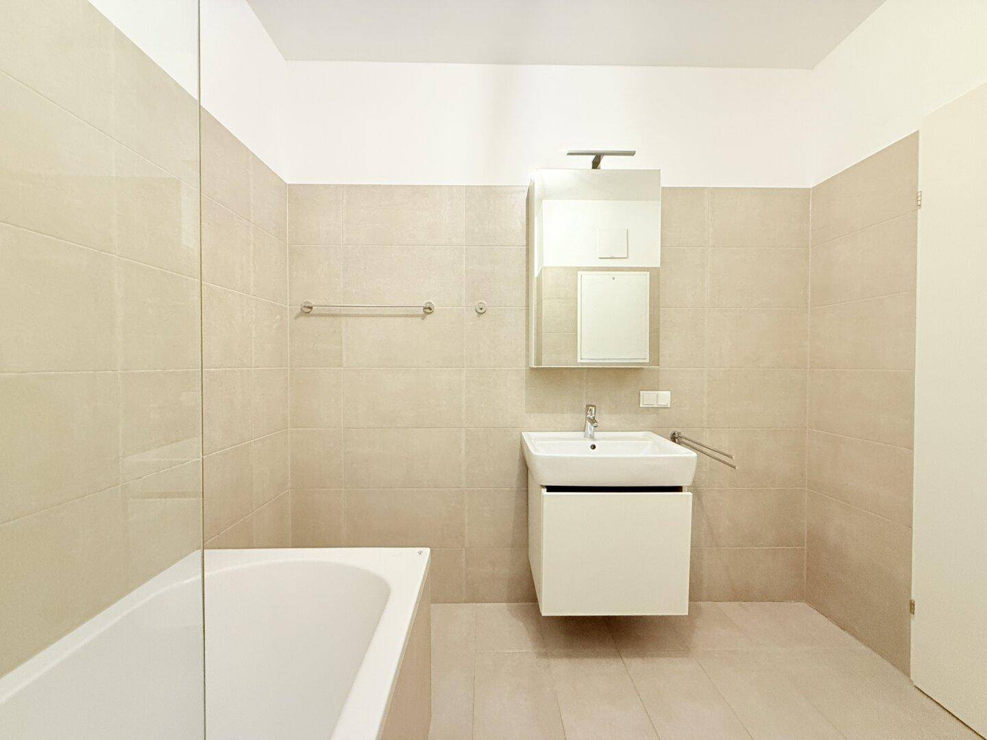 Badezimmer mit modernem Waschtisch, Spiegel und beigefarbenen Wand- und Bodenfliesen.