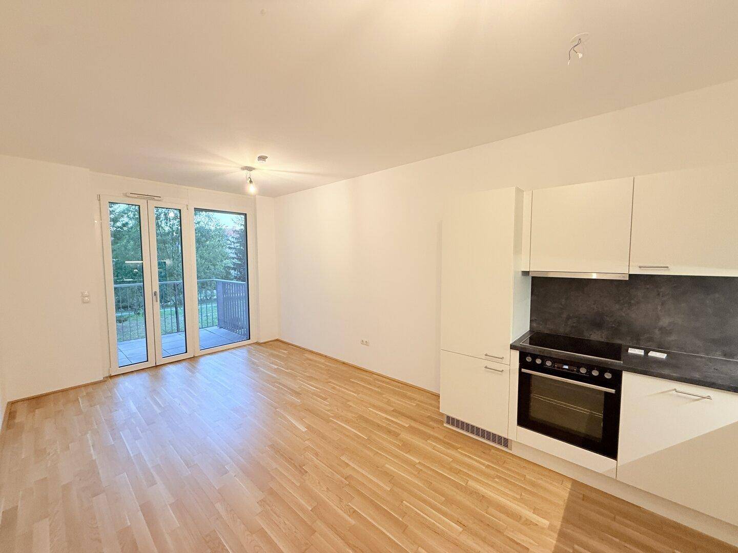 Heller Wohnbereich mit Küchenzeile und direktem Zugang zum Balkon.
