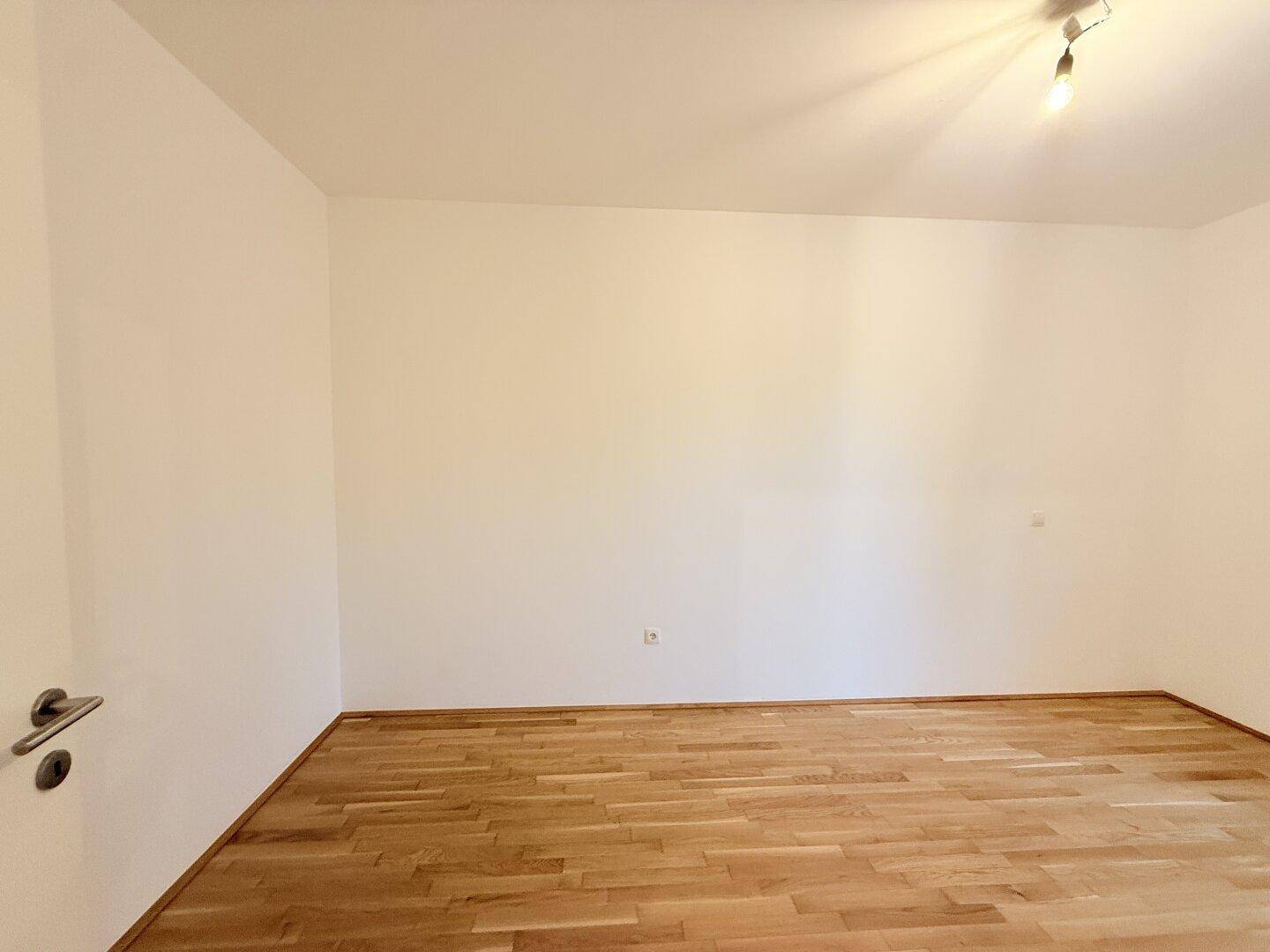 Leerer Raum mit hellem Parkettboden und frisch gestrichenen weißen Wänden.