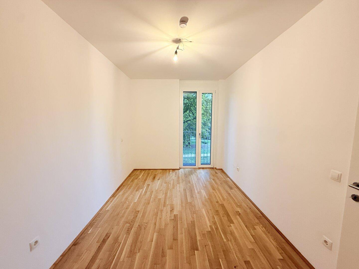 Helles Schlafzimmer mit Parkettboden und Zugang zu einem kleinen Balkon.