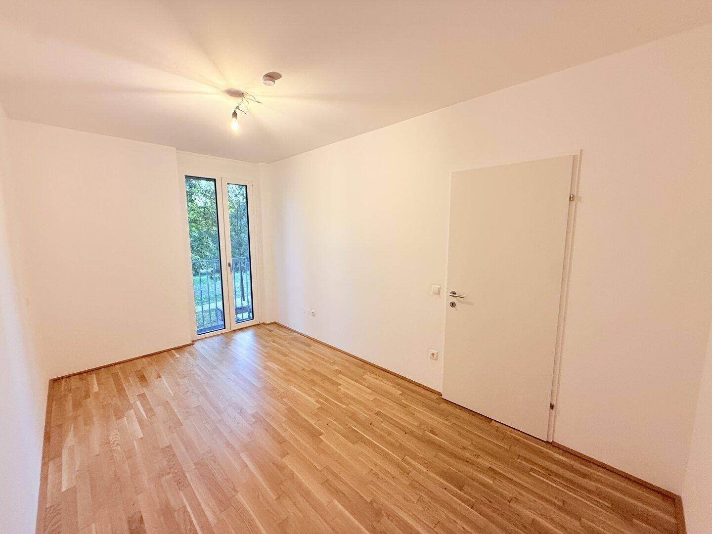 Geräumiges Schlafzimmer mit Parkettboden, weißen Wänden und Balkonzugang.