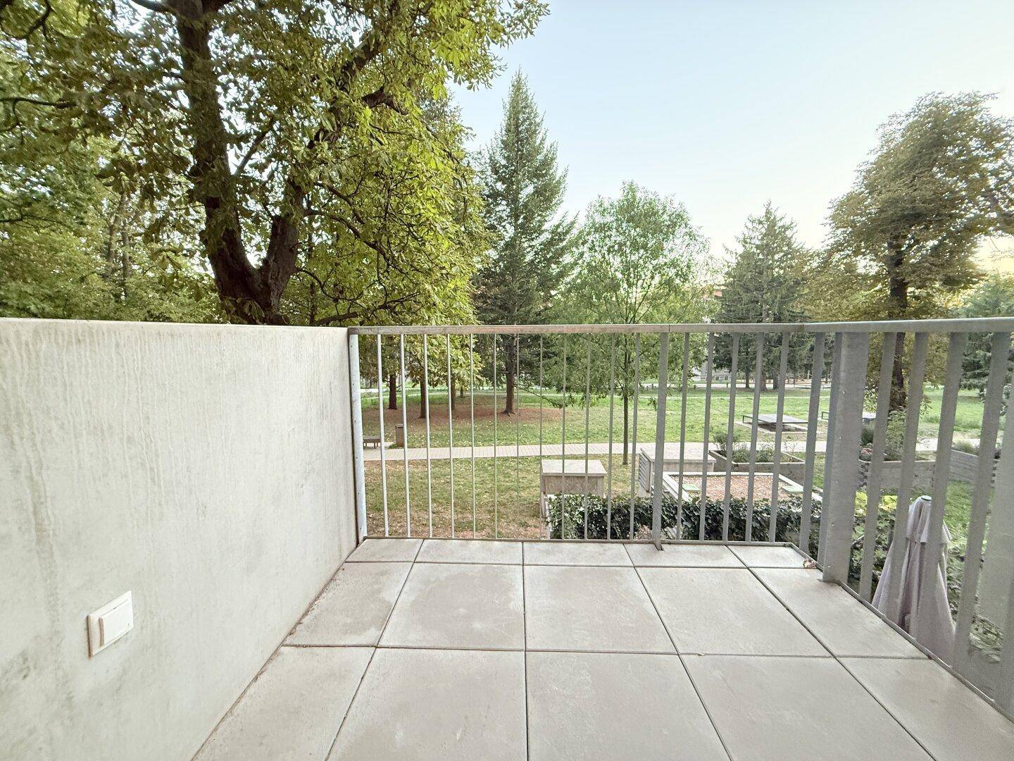 Moderner Balkon mit Fliesenboden und Blick auf eine grüne Parkanlage.
