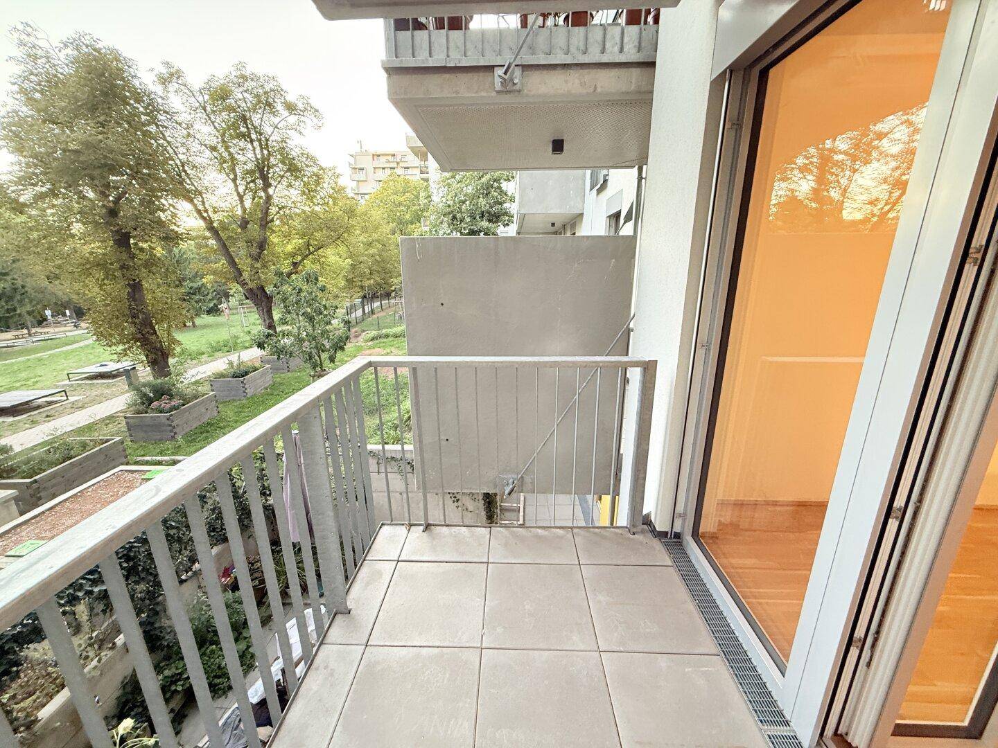 Heller Balkon mit Fliesen und Metallgeländer, bietet Aussicht auf Bäume und Nachbargebäude.