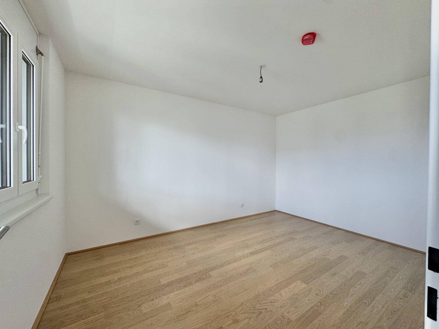 Leeres Zimmer mit hellem Parkettboden und großem Fenster, ideal als Schlafzimmer.