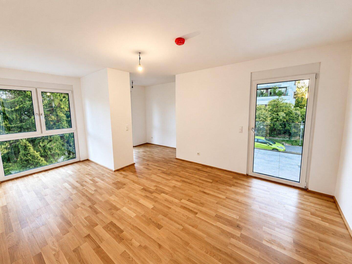 Heller Wohnraum mit Eichenparkettboden, weißen Wänden und großen Fenstern mit Blick ins Grüne.