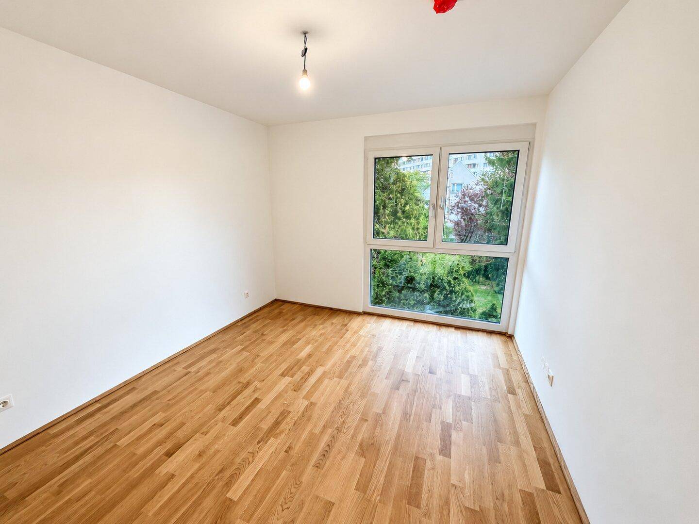 Ruhiges Schlafzimmer mit hellem Parkettboden und großem Fenster, das viel Tageslicht hereinlässt.