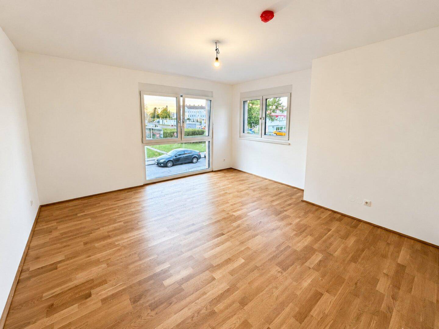Helles Zimmer mit Parkettboden und zwei Fenstern, die einen Blick auf die Straße bieten.