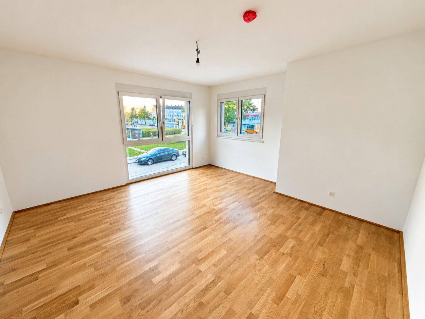 Geräumiges Zimmer mit hellem Parkett und großen Fenstern, die für eine freundliche Atmosphäre sorgen.